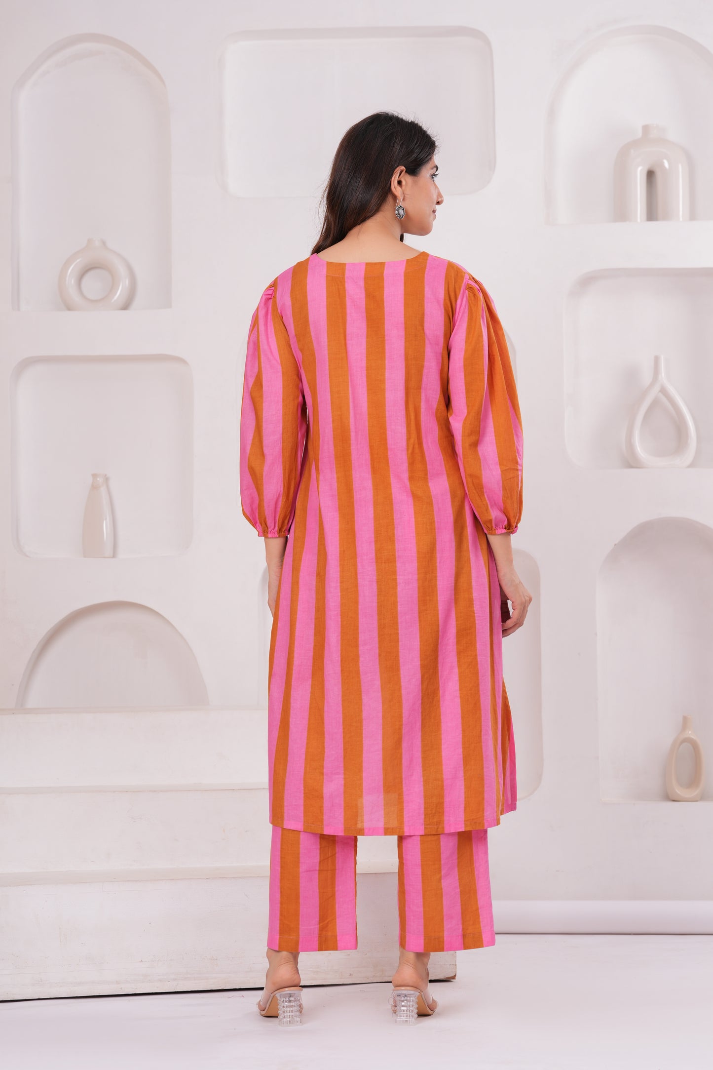 Woman wearing a pink and orange striped outfit against a white geometric background