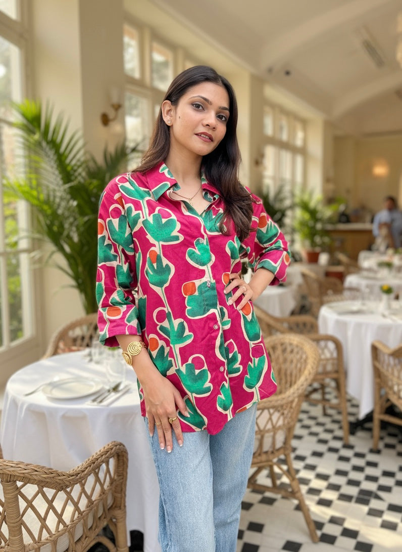 Woman in a colorful shirt standing in a restaurant with tables and chairs.
