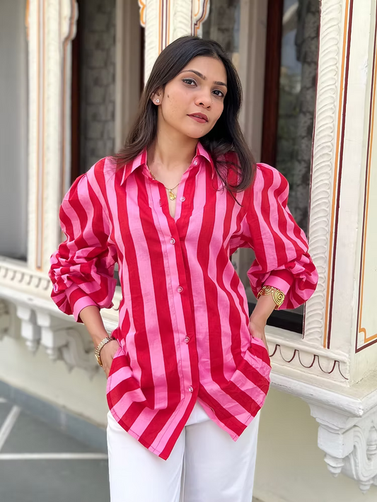 Woman wearing a red and pink striped shirt with white pants, standing in front of an ornate wall.