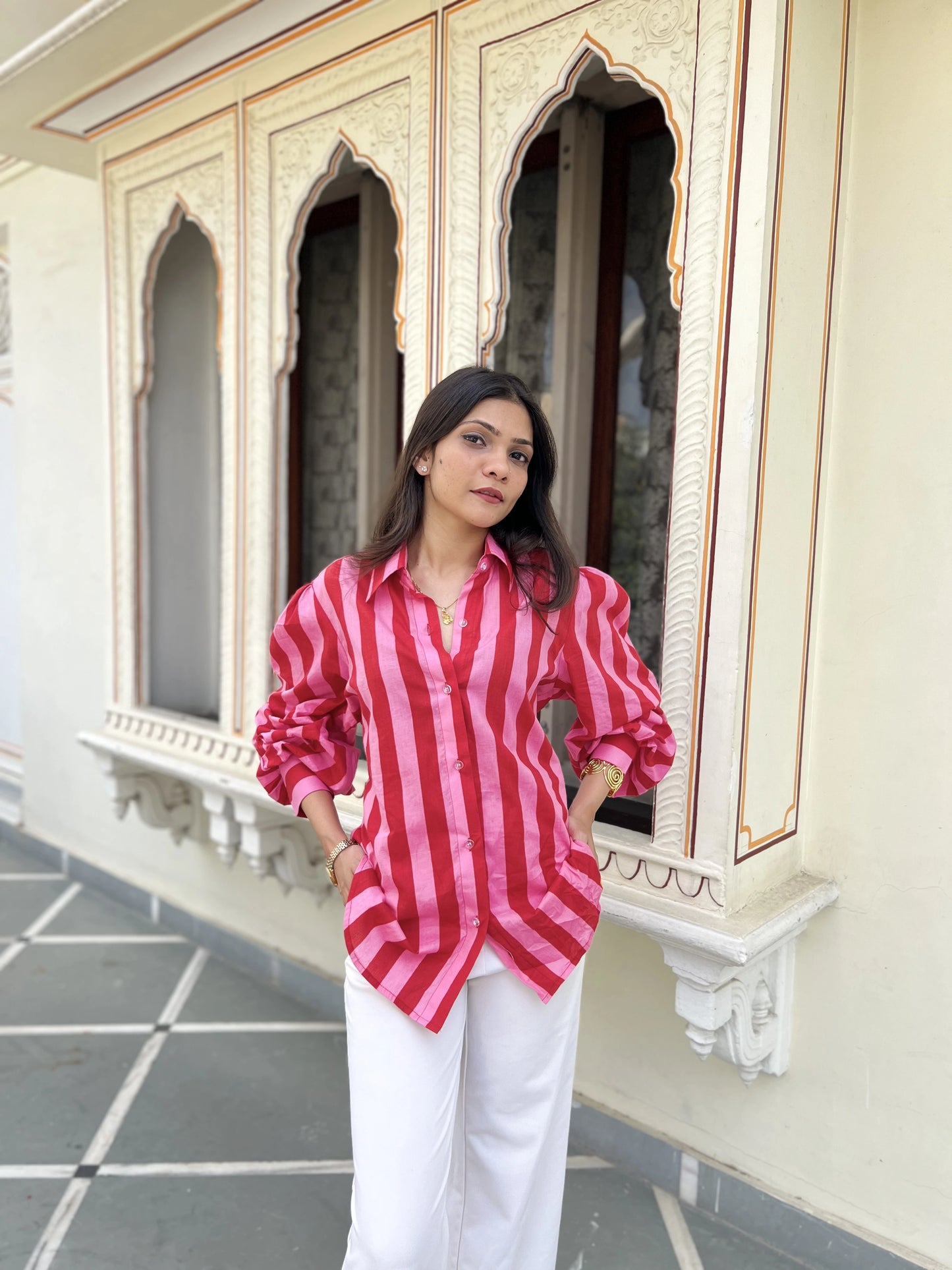 Woman wearing a red and white striped shirt and white pants standing in front of ornate windows.