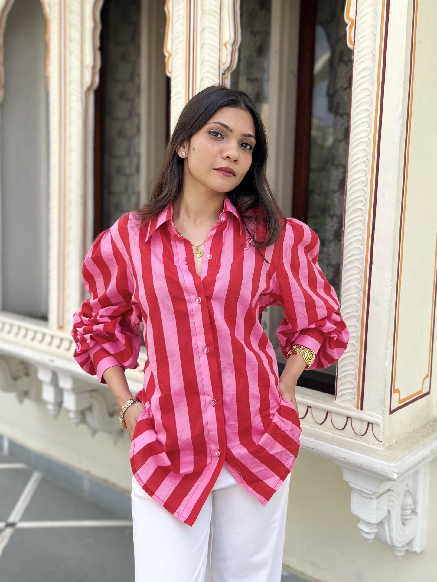 Woman wearing a red and pink striped shirt in front of an ornate building.