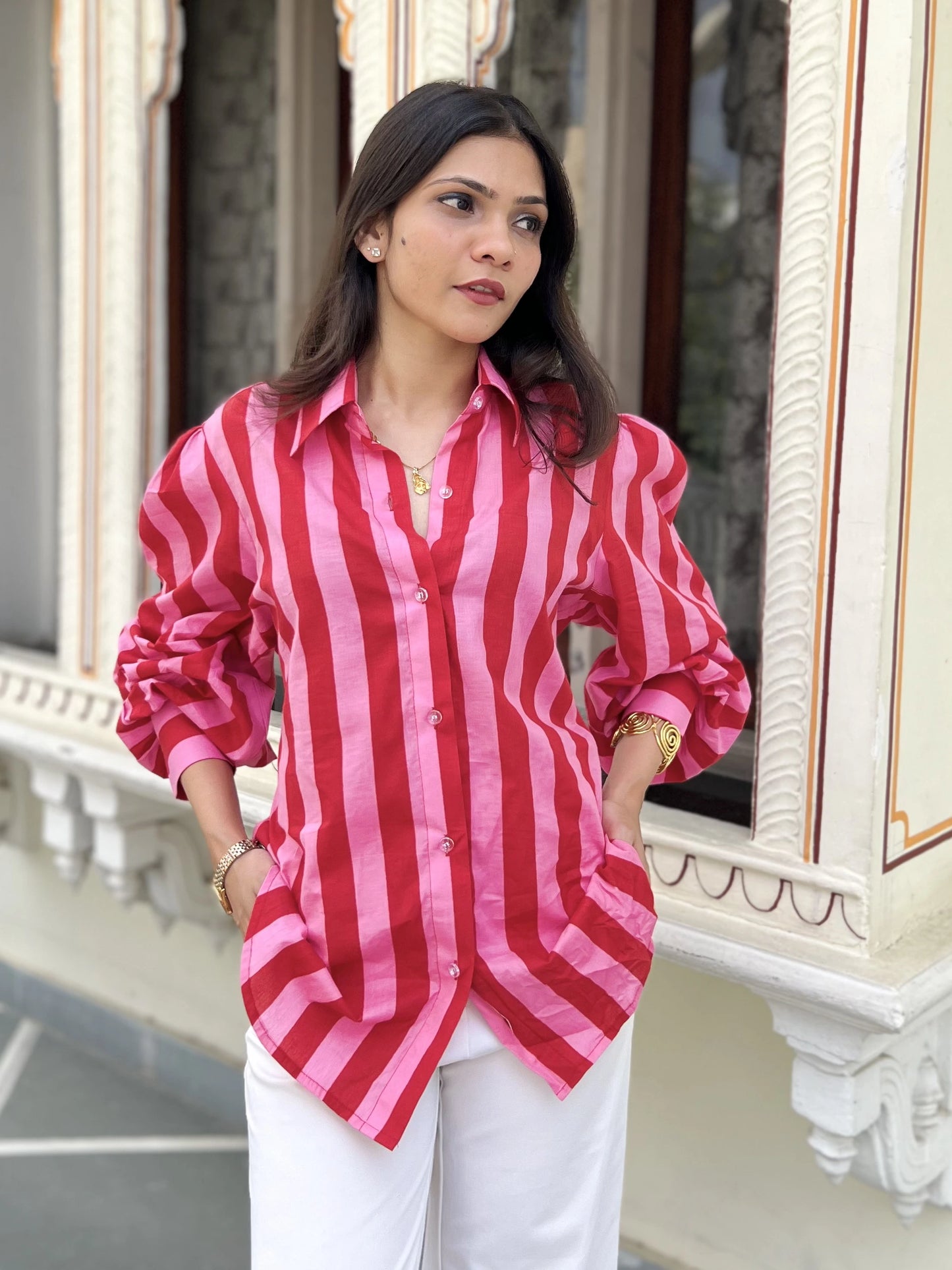 Woman wearing a red and pink striped shirt with white pants standing in front of a decorative window.