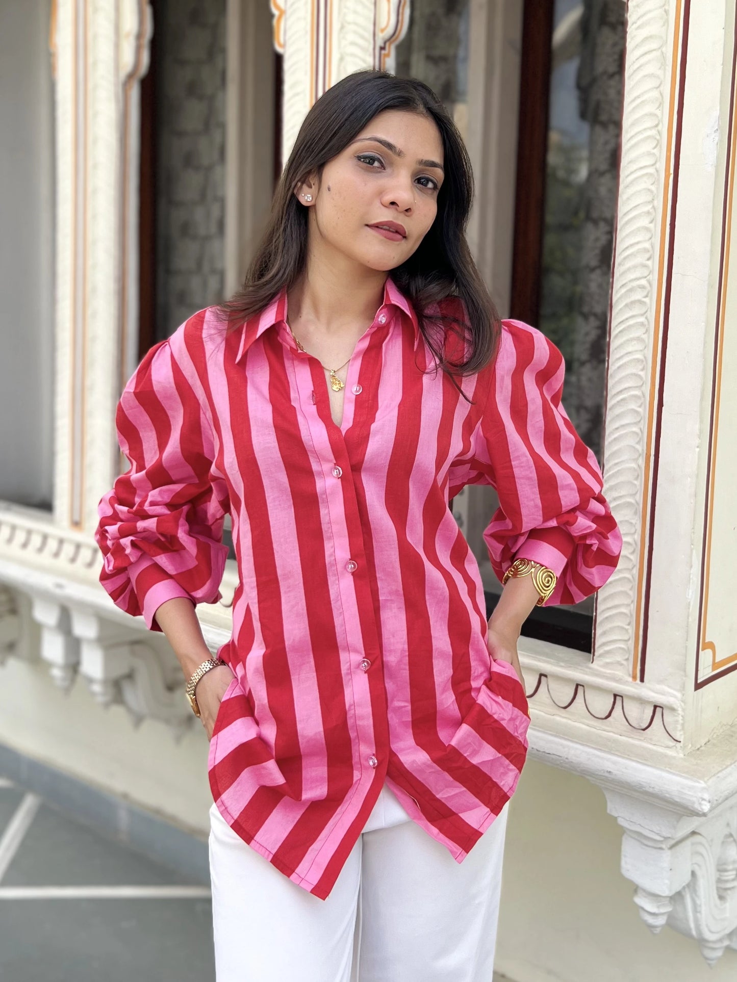 Woman wearing a red and pink striped shirt in front of an ornate building.