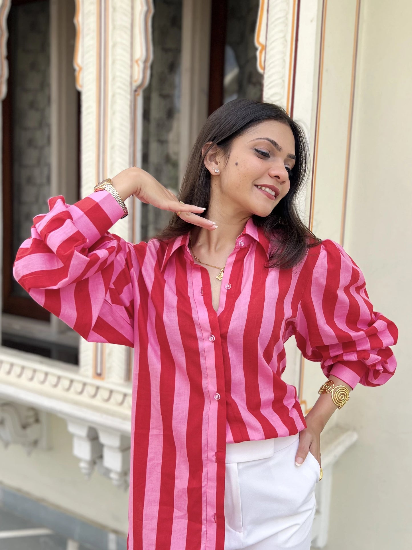 Woman wearing a red and pink striped shirt with white pants, standing in front of a decorative window.