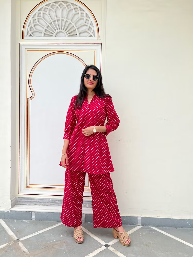 Woman in a red lehariya outfit standing in front of an ornate archway.