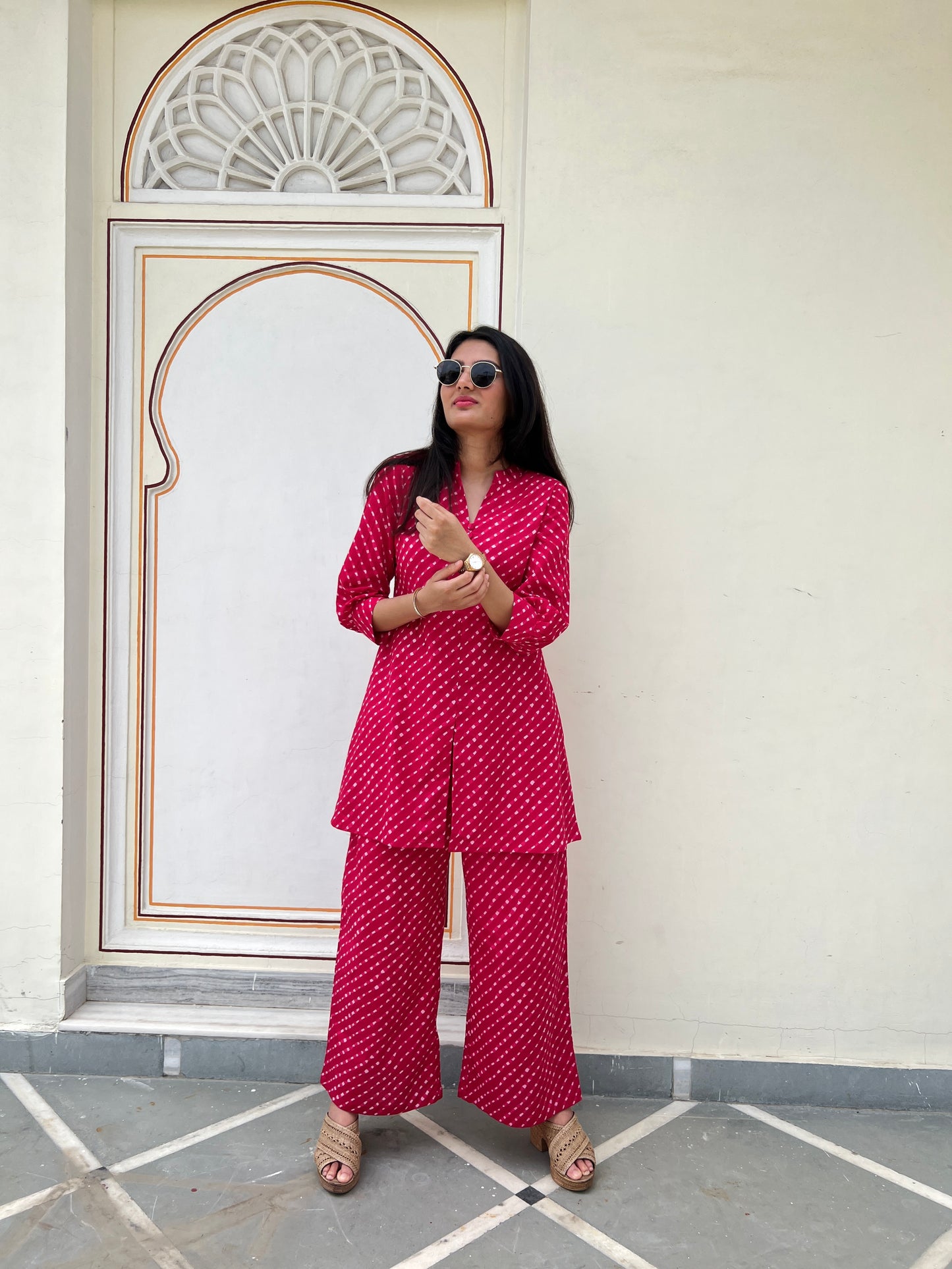 Woman in a red patterned outfit standing in front of a decorative archway.