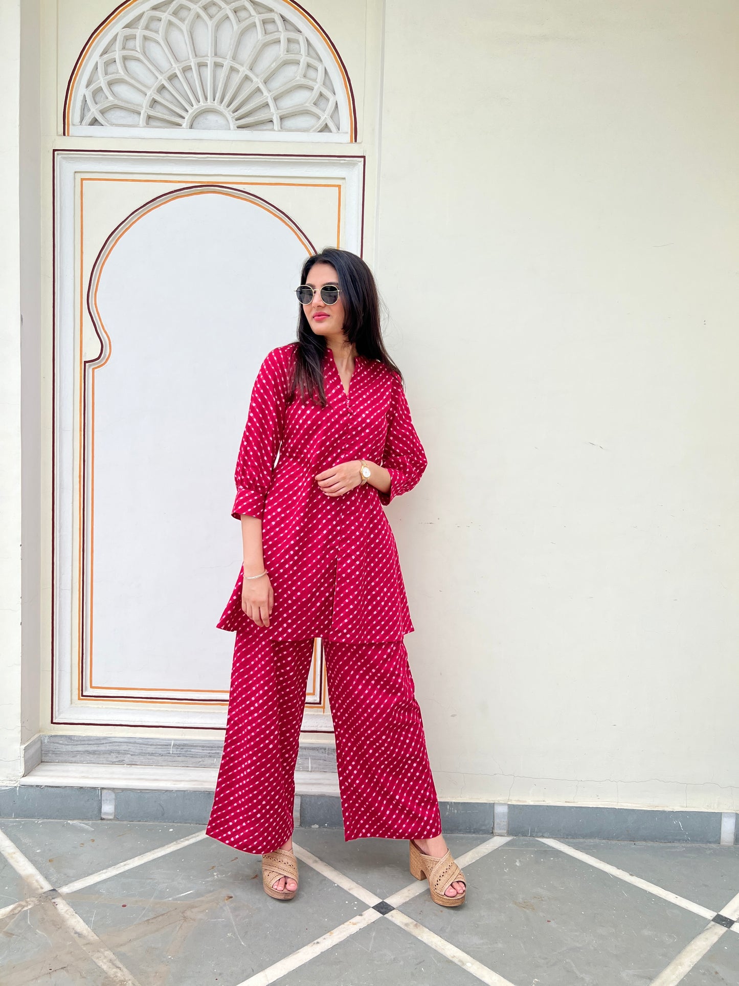 Woman in a red patterned outfit standing in front of a decorative wall.