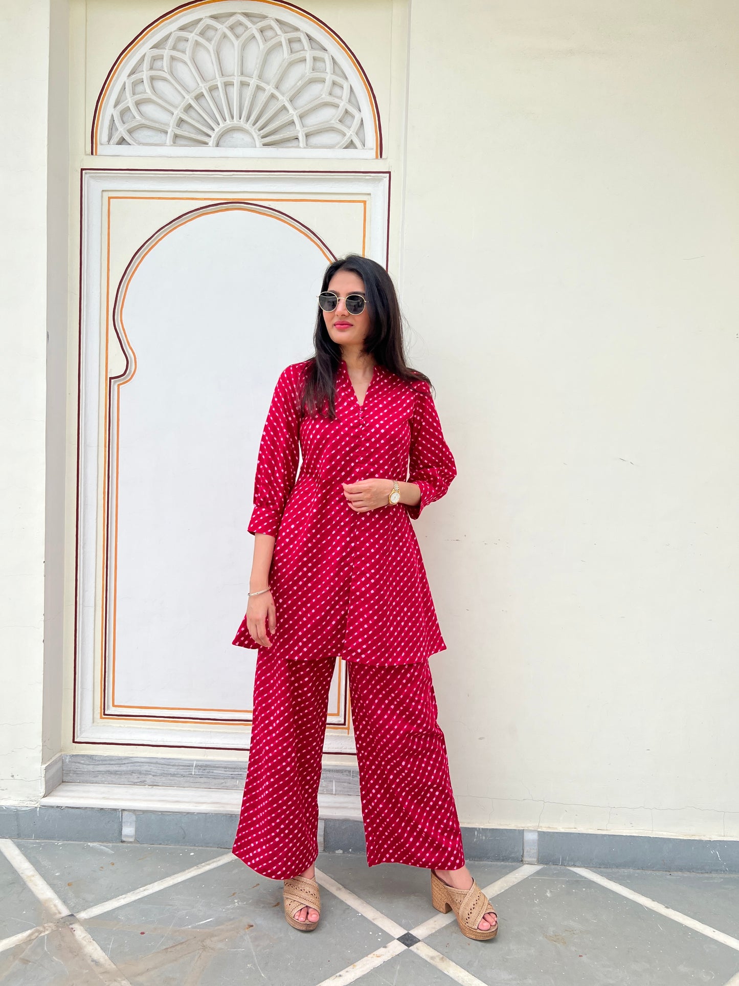 Woman in a red patterned outfit standing in front of a decorative wall.
