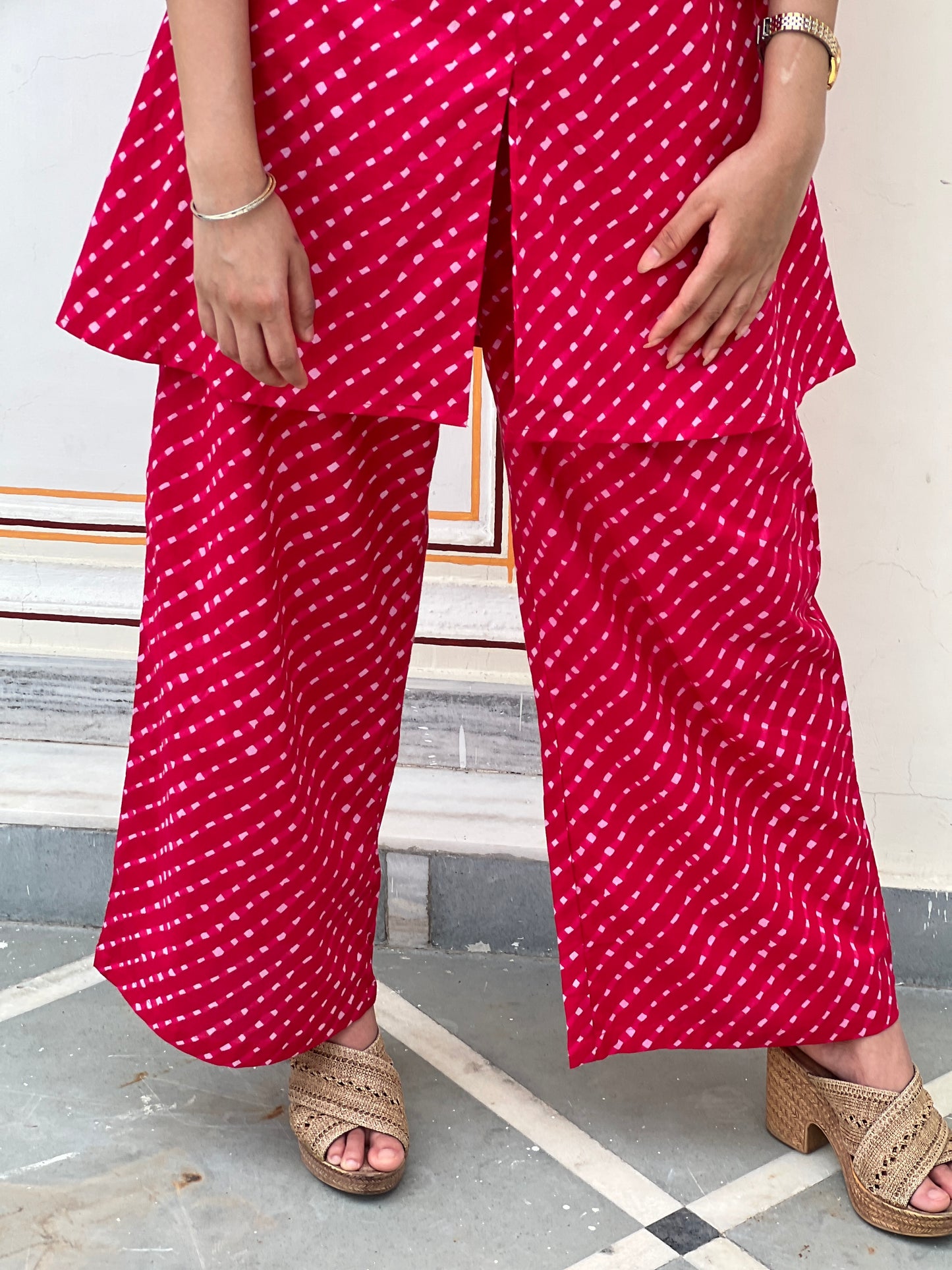 Person wearing a red and white patterned outfit with wide-leg pants indoors.