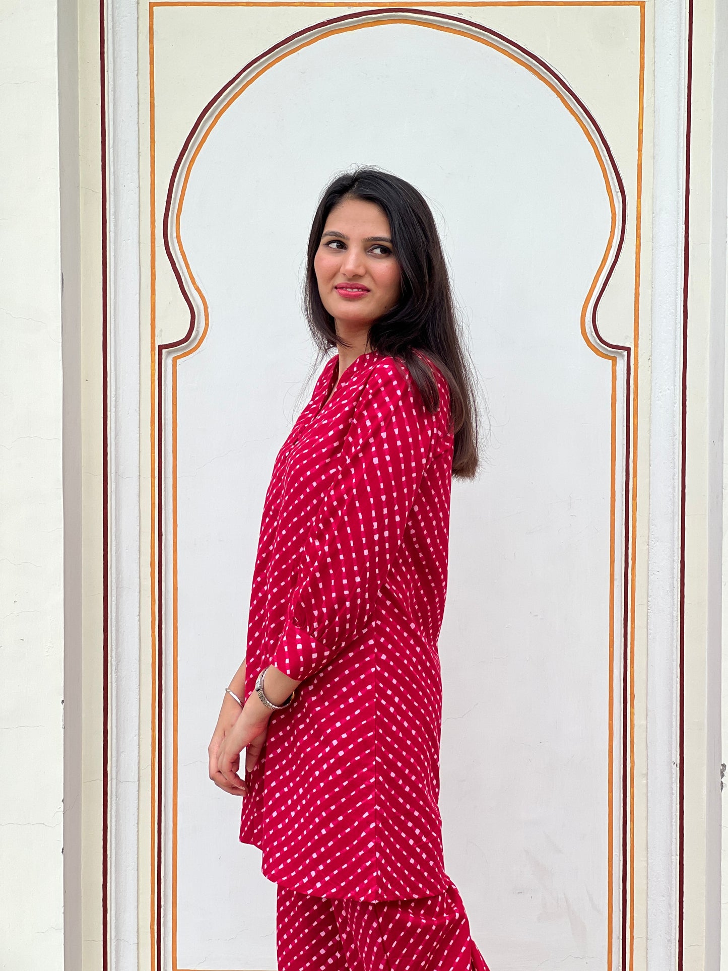 Woman wearing a red polka dot outfit standing in front of a decorative wall.