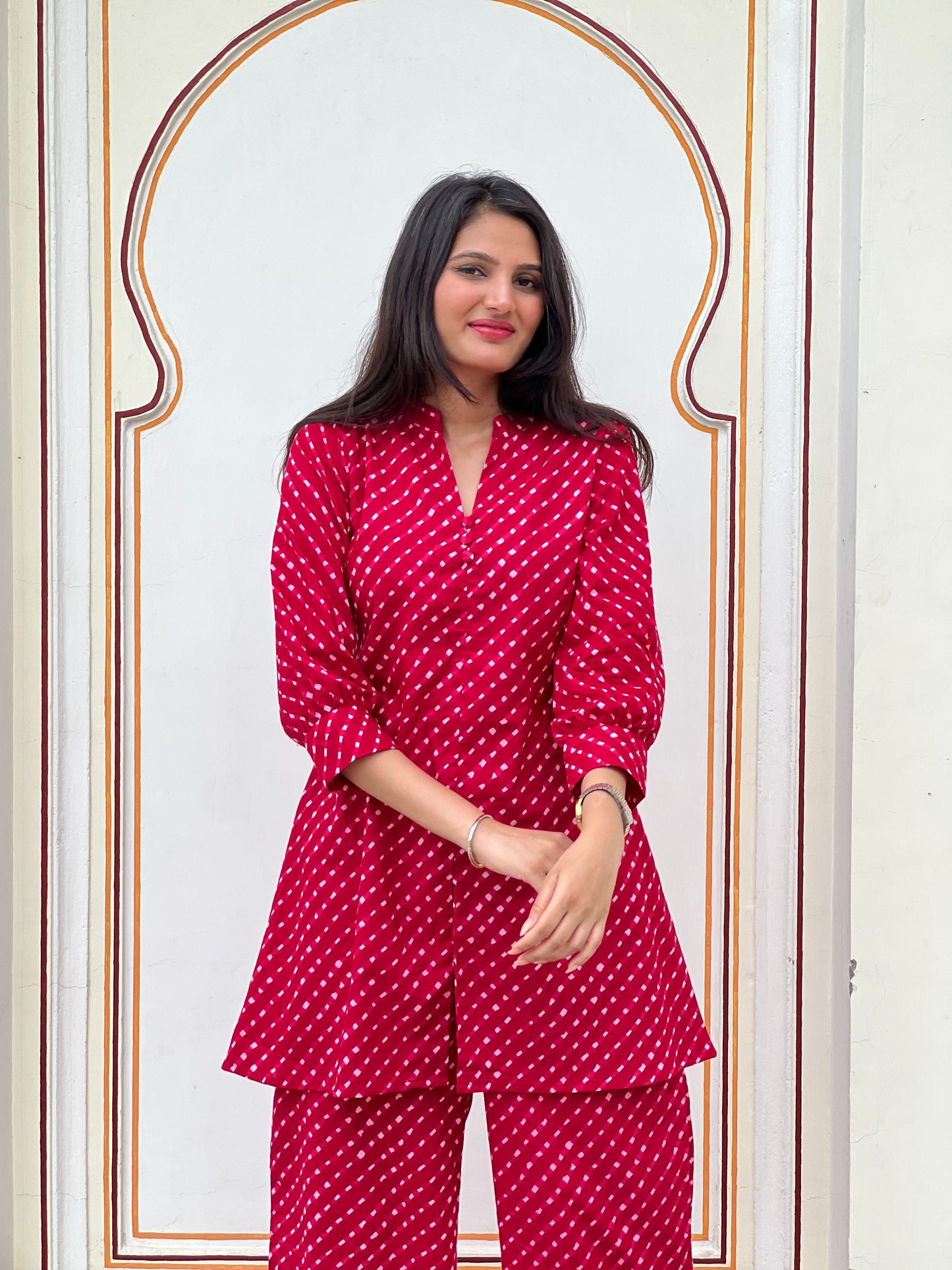 Woman wearing a red lehariya outfit standing in front of a decorative wall.