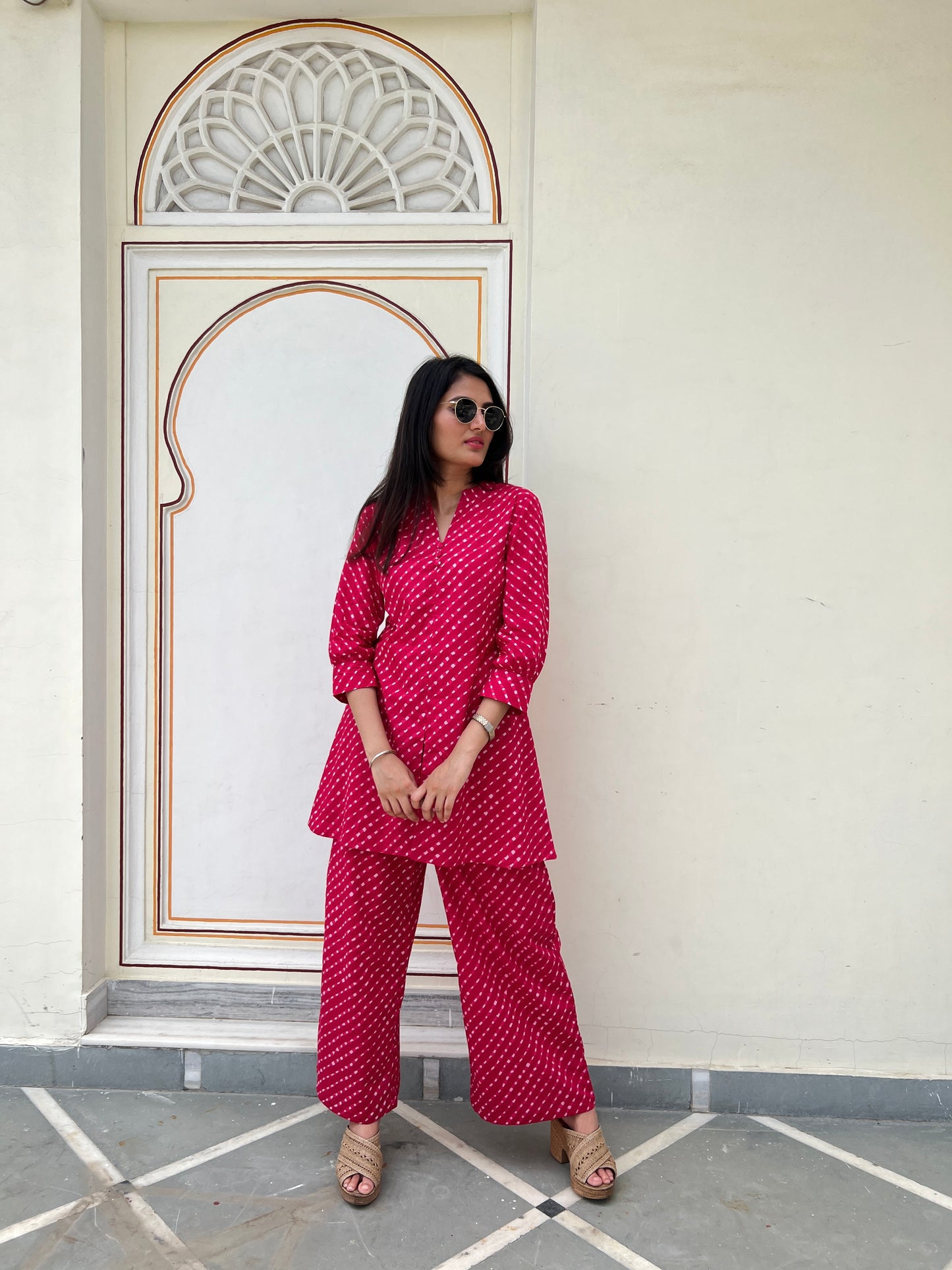Woman in a red patterned outfit standing in front of a decorative wall.
