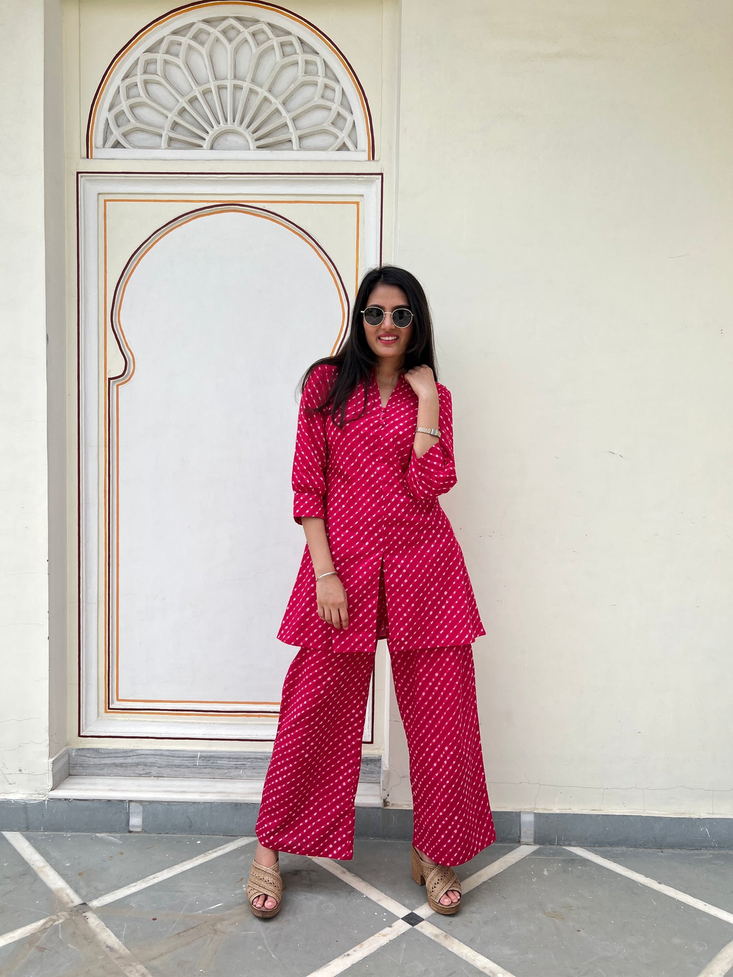 Woman in a red patterned outfit standing in front of a decorative wall.