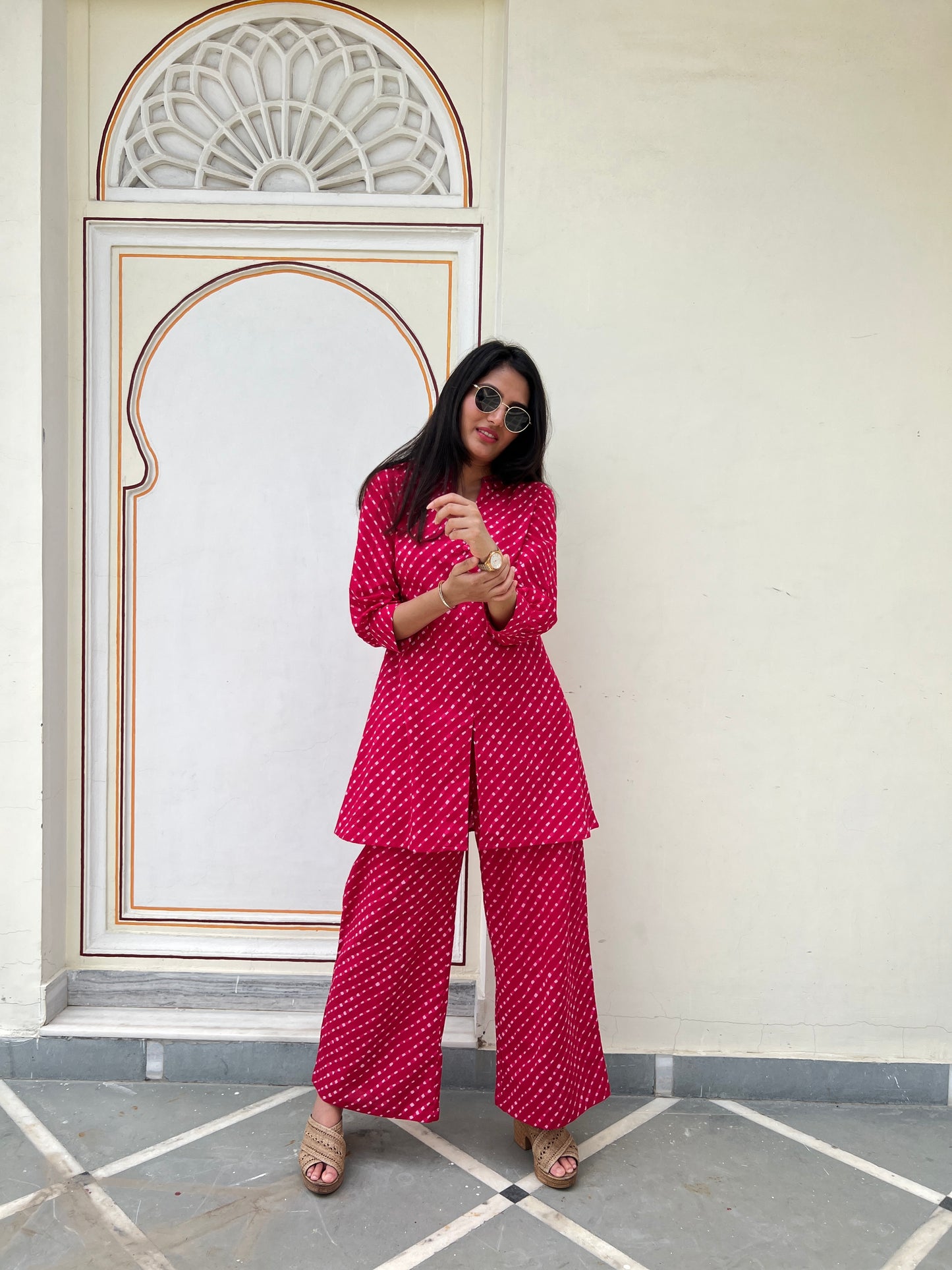 Woman in a red patterned outfit standing in front of a decorative wall.