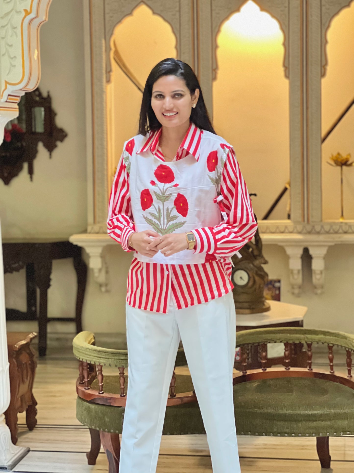 Woman wearing a red and white patterned shirt with a floral design in an ornate room.