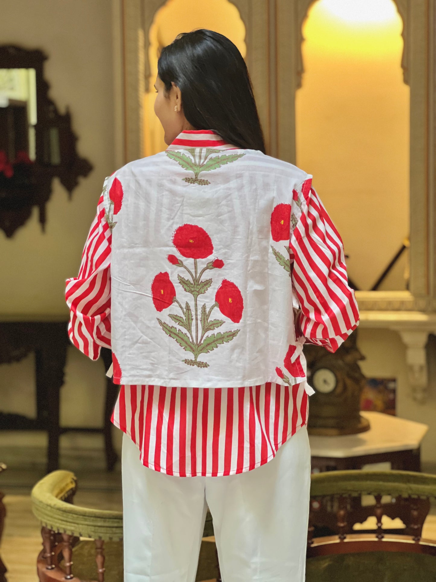 Person wearing a red and white striped shirt with floral embroidery in a room.