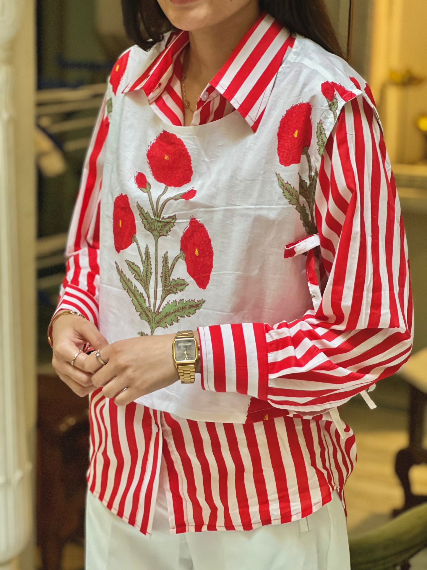 Person wearing a red and white striped shirt with floral embroidery indoors.