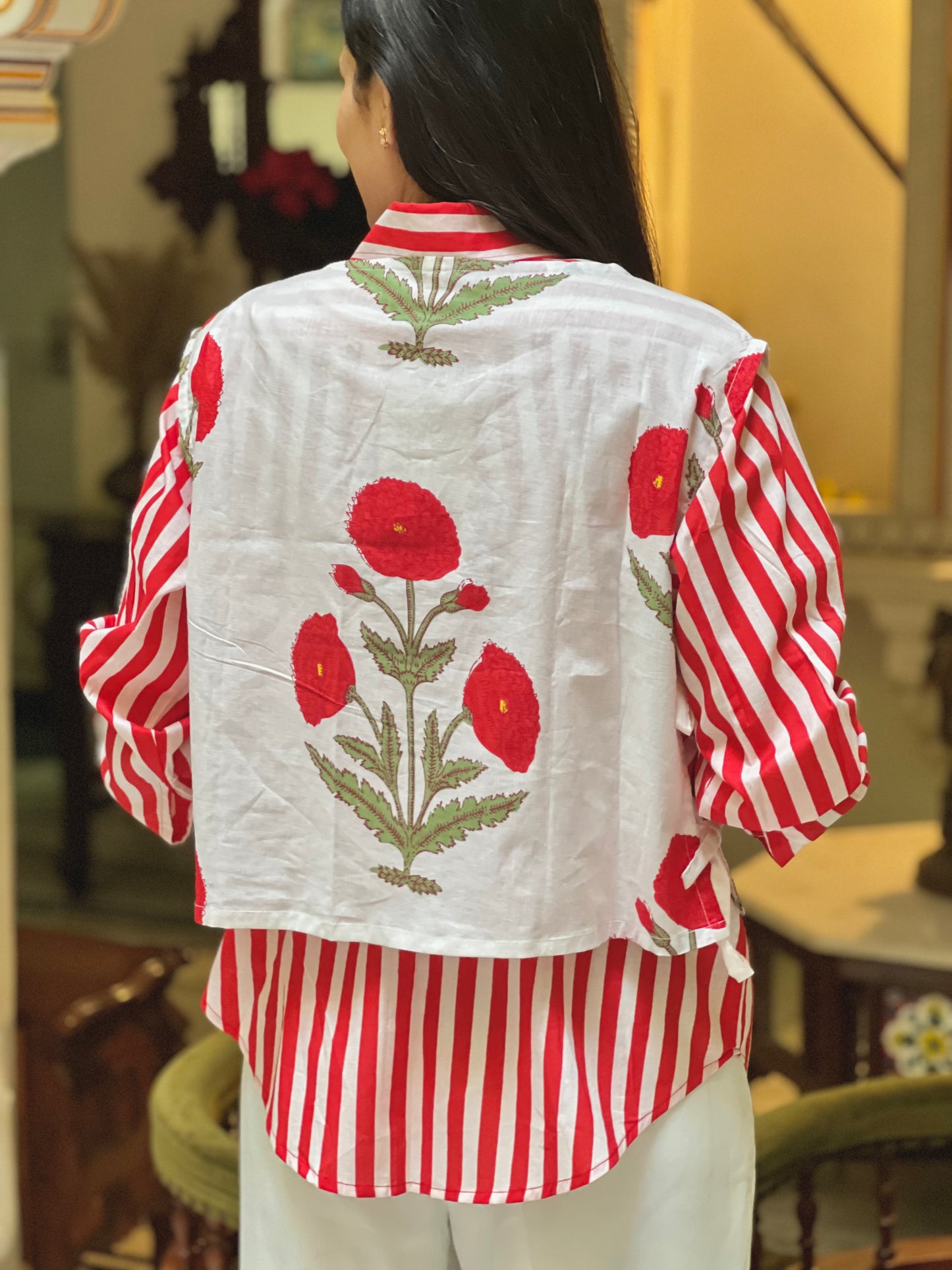 Person wearing a white shirt with red floral embroidery and a red and white striped vest.