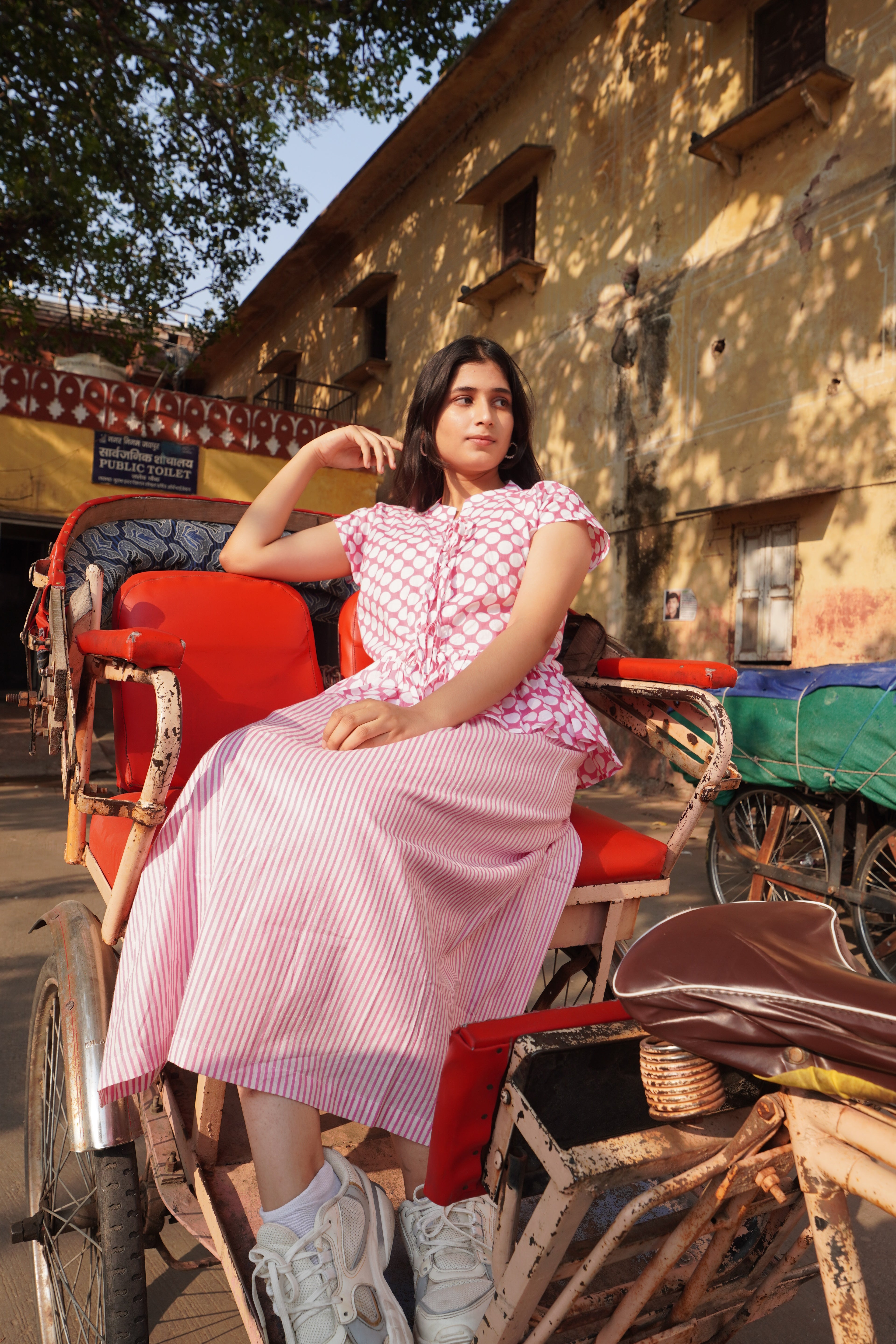 Woman in a pink dress sitting on a red rickshaw in an urban setting