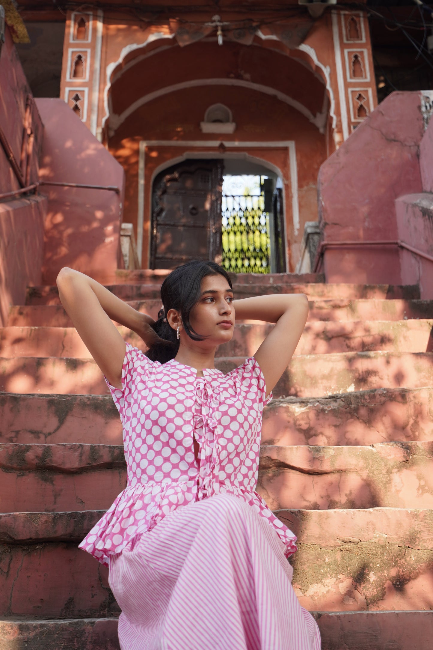 Woman in a pink polka dot dress sitting on steps with a historical building in the background