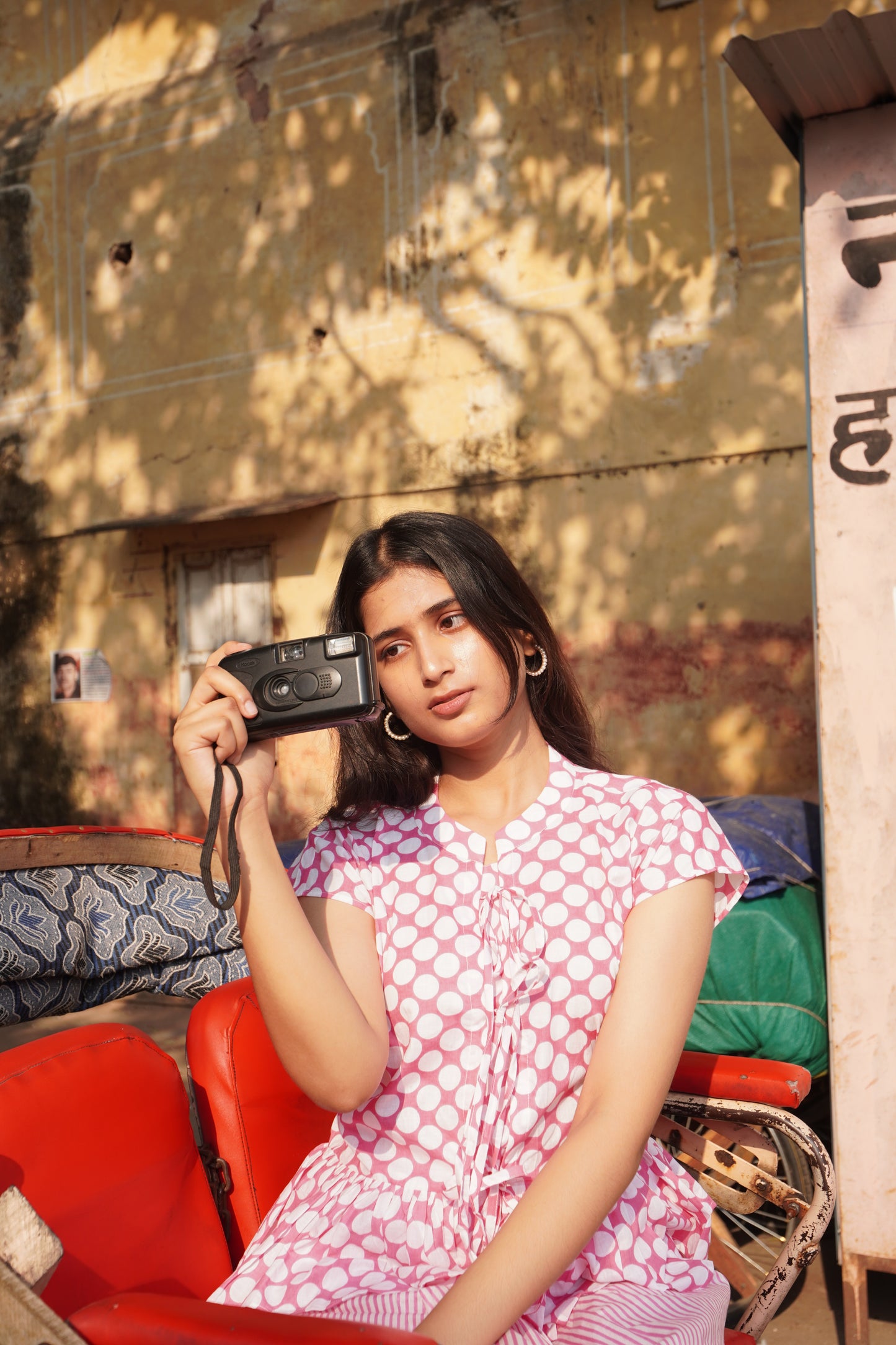 Woman in a polka dot dress holding a camera outdoors.