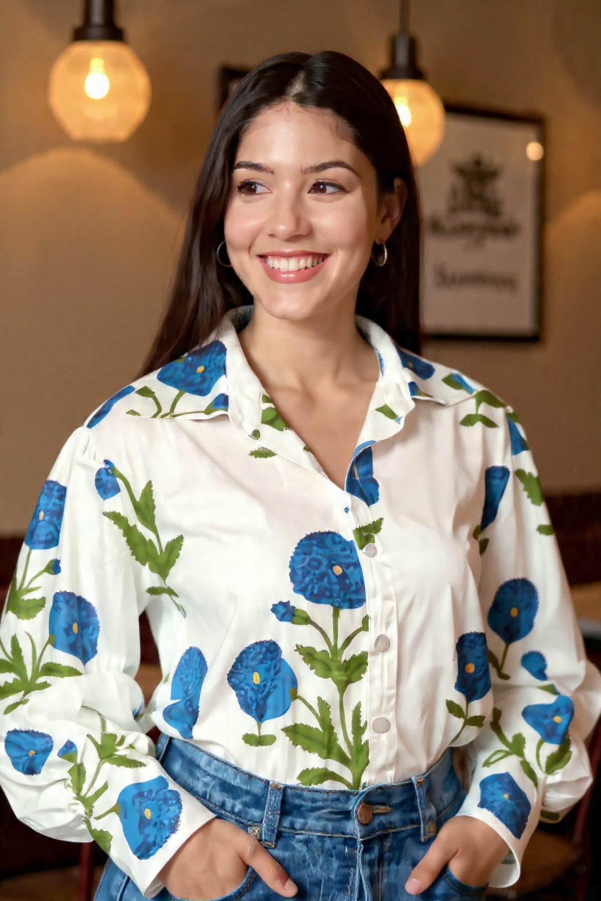 Woman wearing a white blouse with blue floral patterns in an indoor setting.