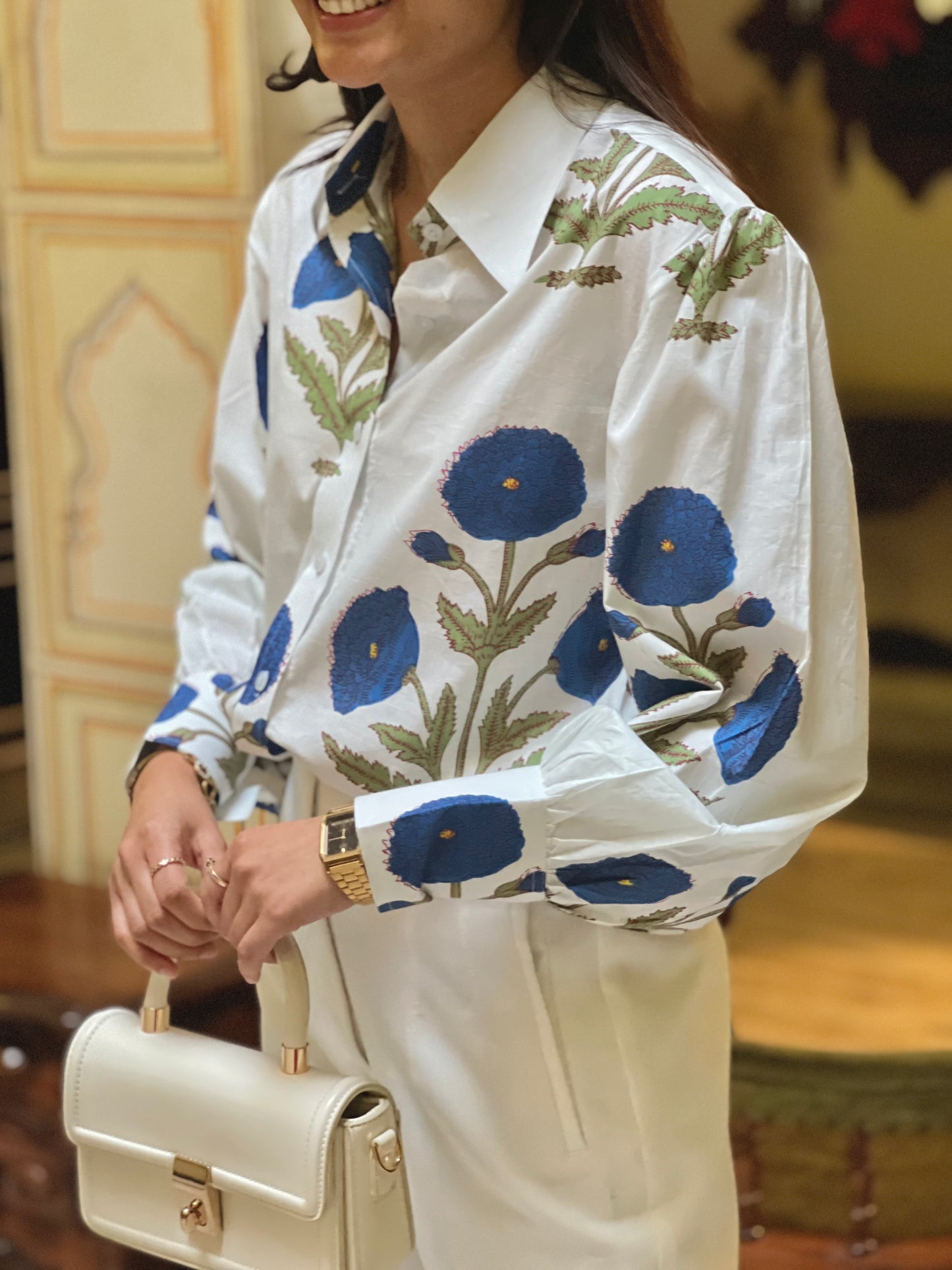 Person wearing a white shirt with blue floral patterns, holding a beige handbag.