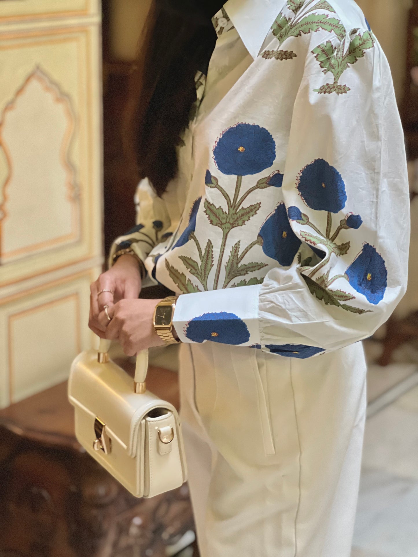 Person wearing a floral embroidered jacket holding a beige handbag.