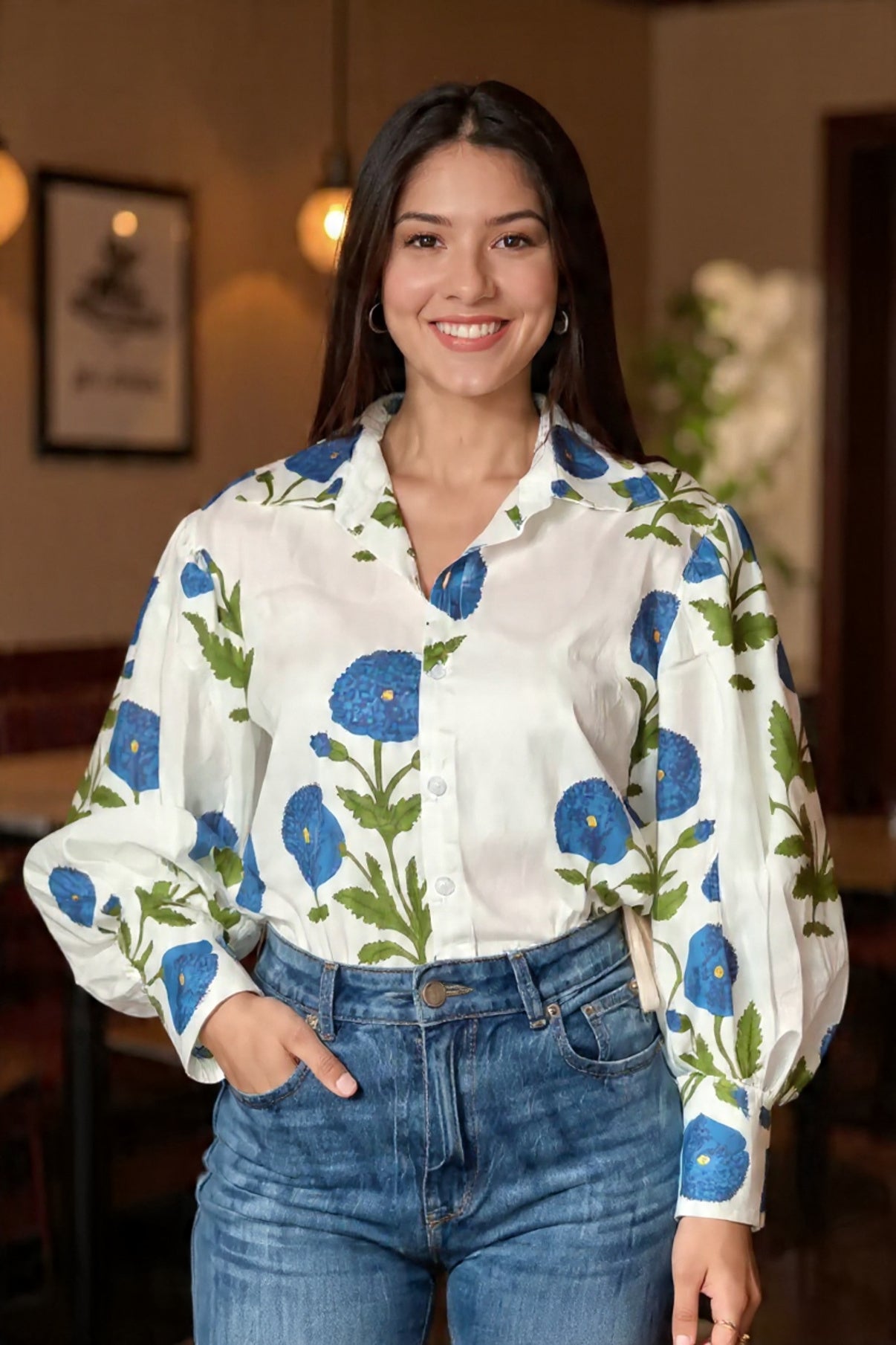 Woman wearing a white blouse with blue floral patterns and blue jeans indoors.