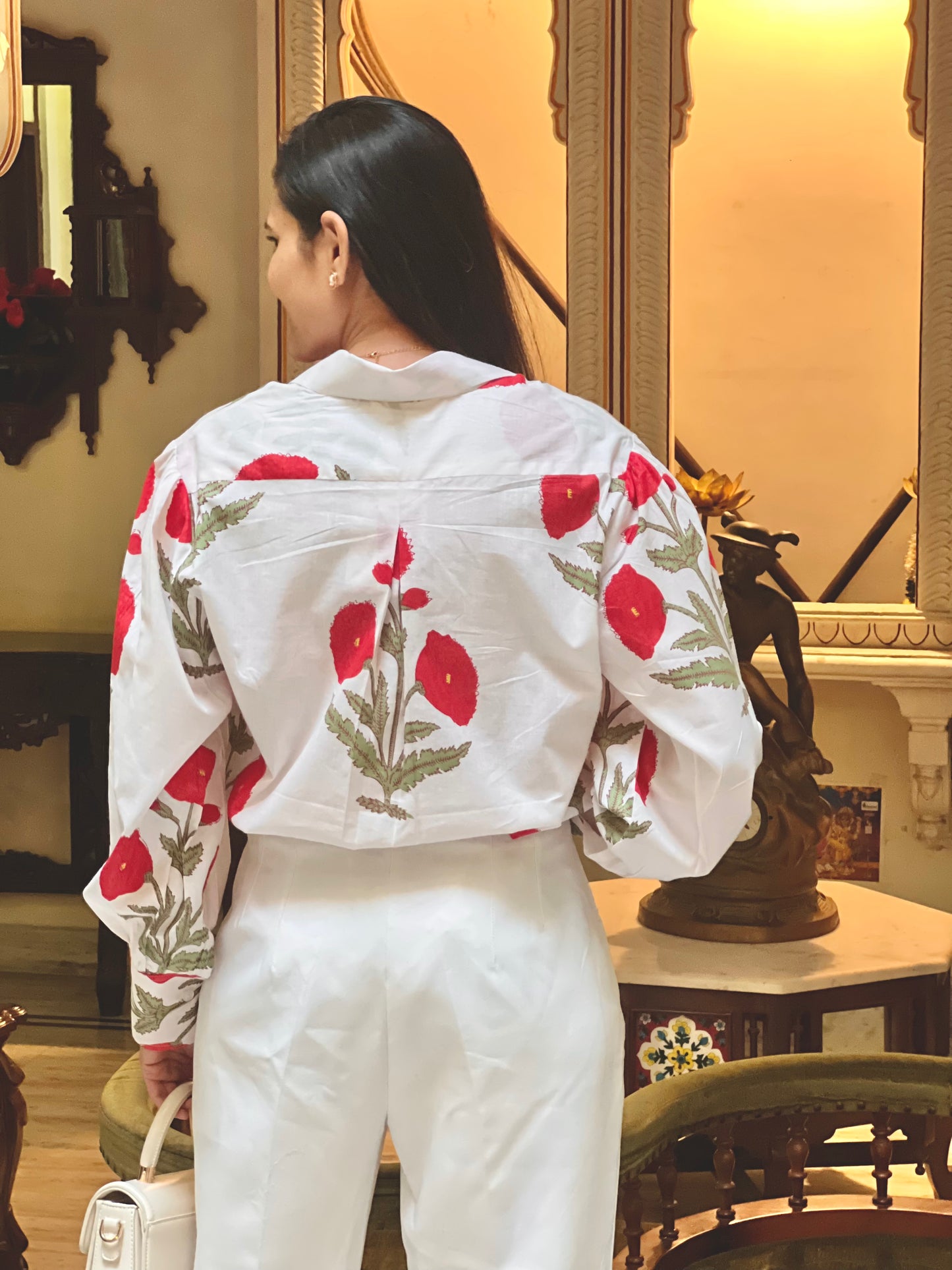 Woman wearing a white blouse with red floral patterns in an indoor setting.