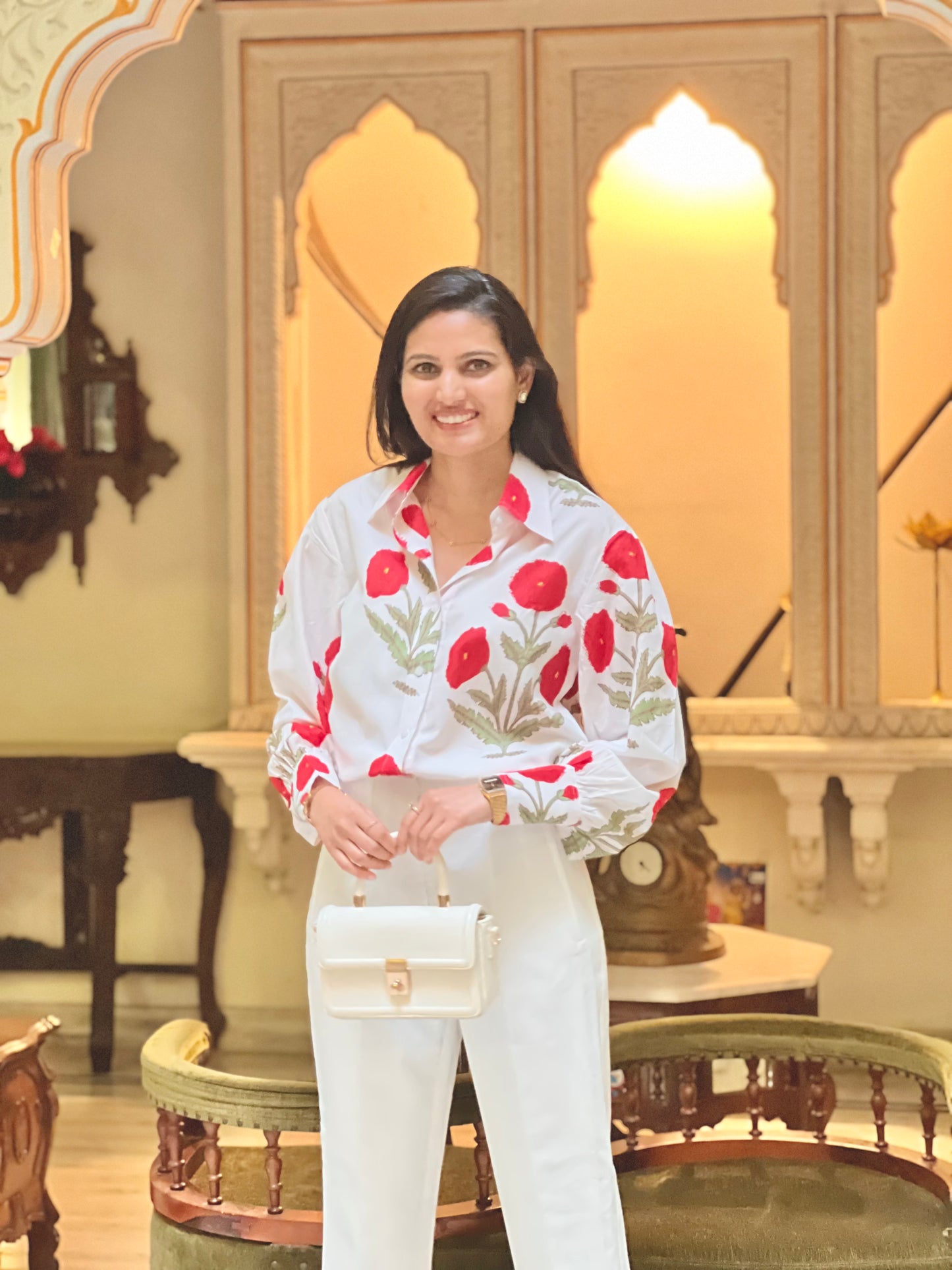 Woman in a white outfit with red floral patterns standing in an ornate room.