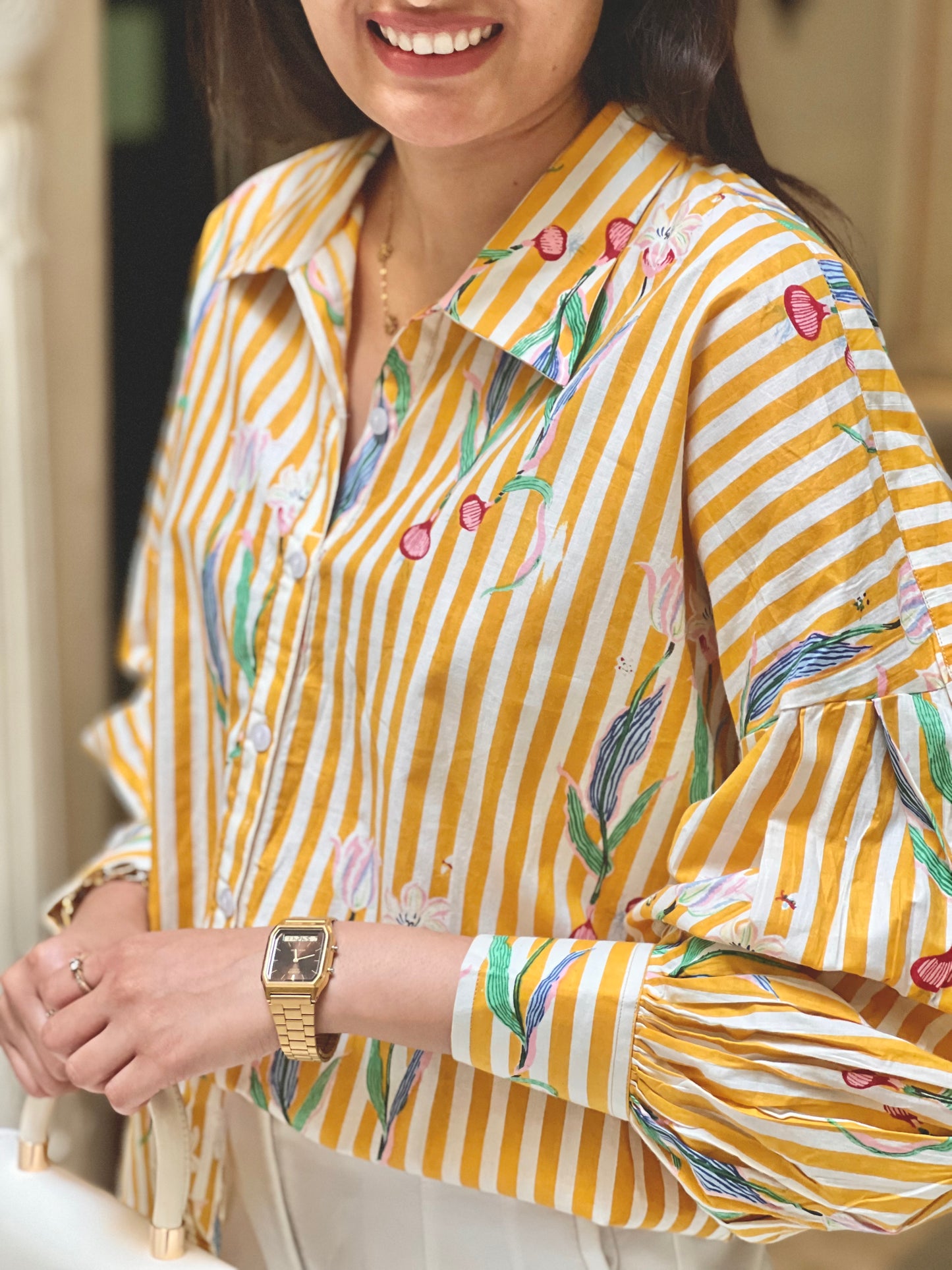 Woman wearing a yellow and white striped shirt with floral patterns, smiling.