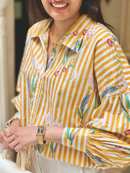 Woman wearing a yellow and white striped shirt with floral patterns, smiling.