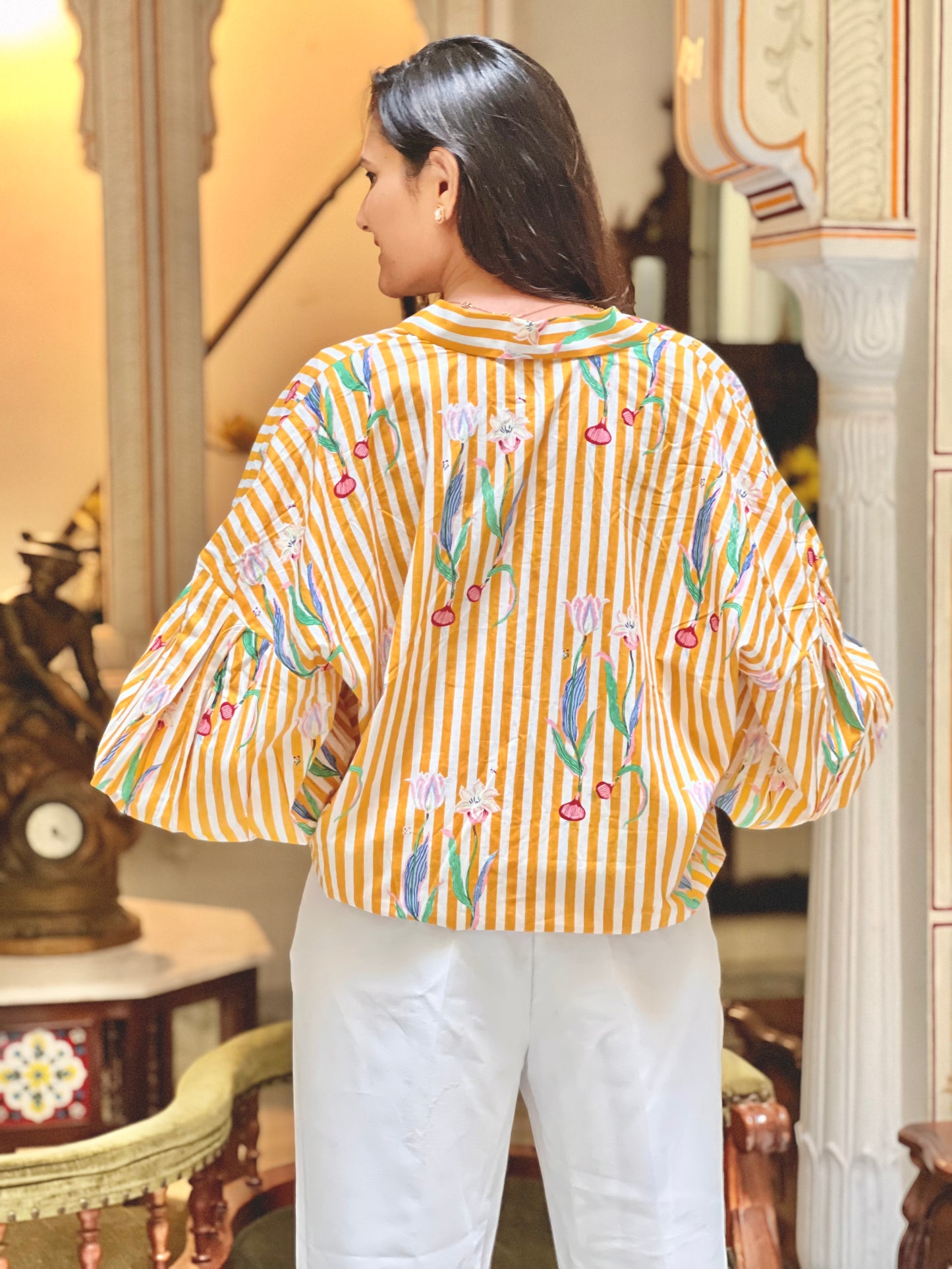 Woman wearing a yellow and white striped shirt with floral patterns in an indoor setting.