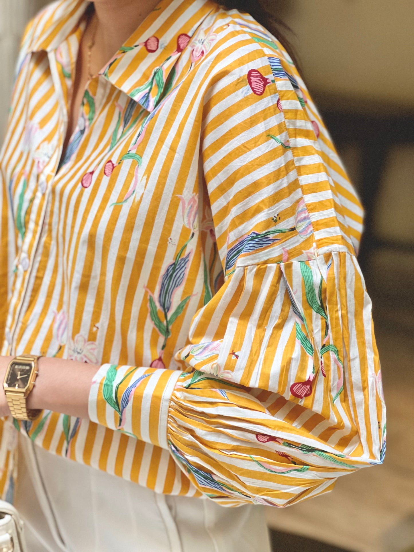 Yellow and white striped shirt with floral patterns worn by a person.