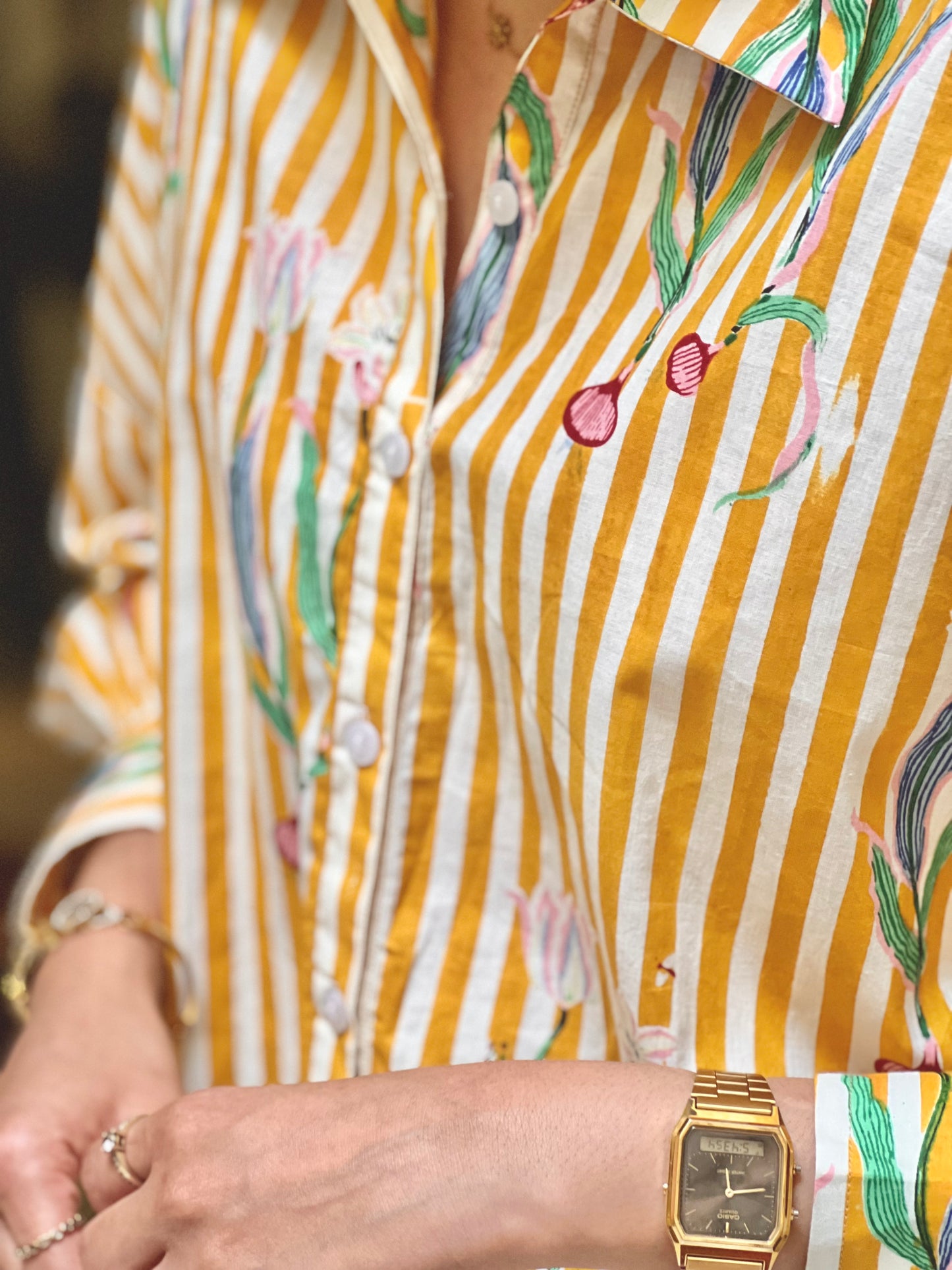 Close-up of a person wearing a yellow striped shirt with floral patterns and a gold watch.