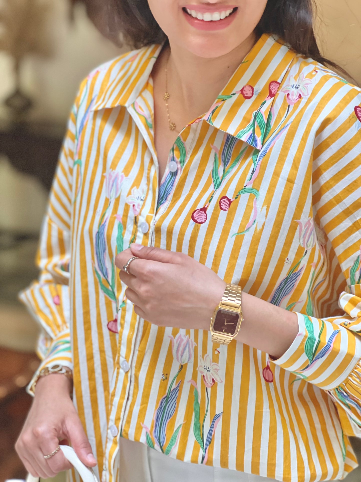 Person wearing a yellow and white striped shirt with floral embroidery, holding a phone.