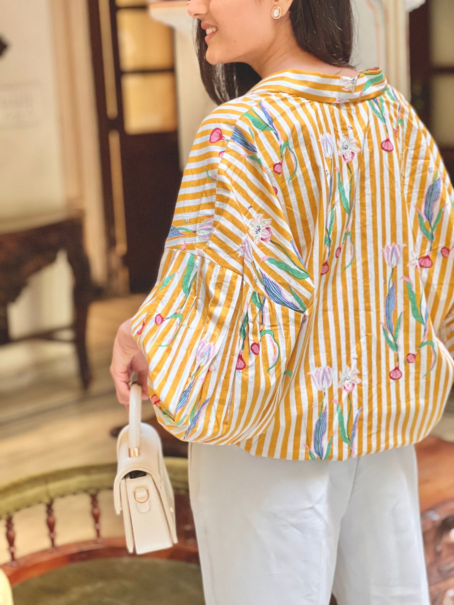 Woman wearing a yellow and white striped shirt with floral patterns indoors.
