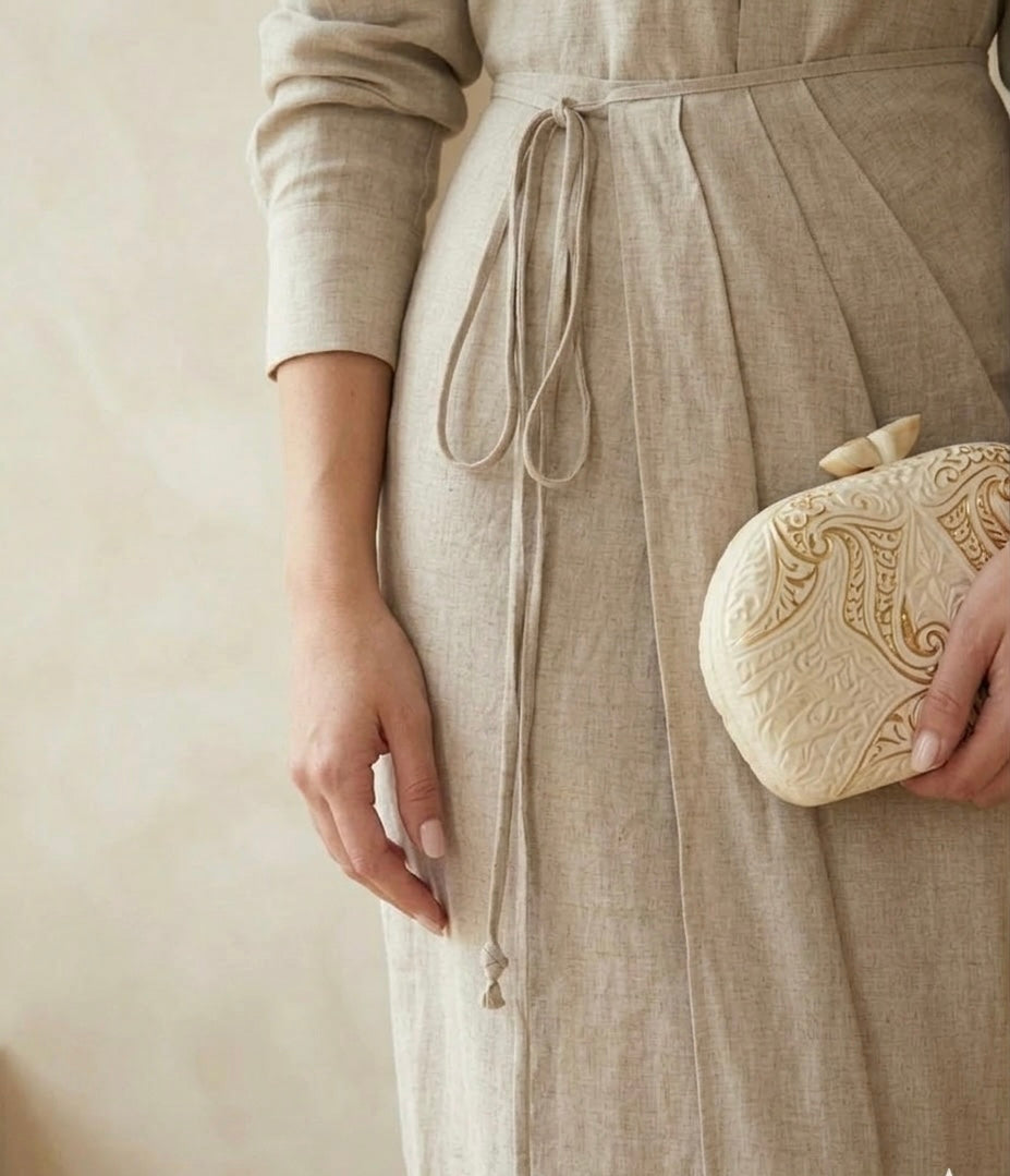 Person wearing a beige dress holding a matching clutch against a plain background