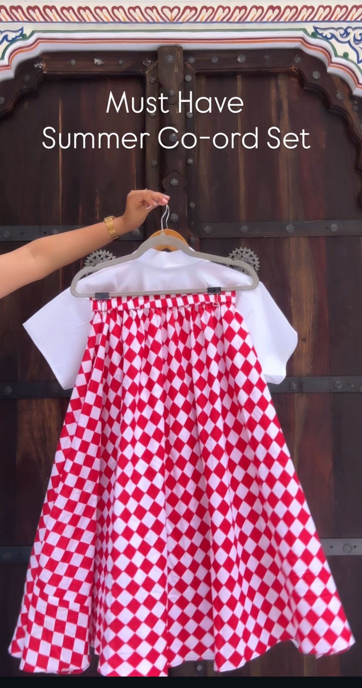 Red and white checkered skirt with white top on hanger against a dark background
