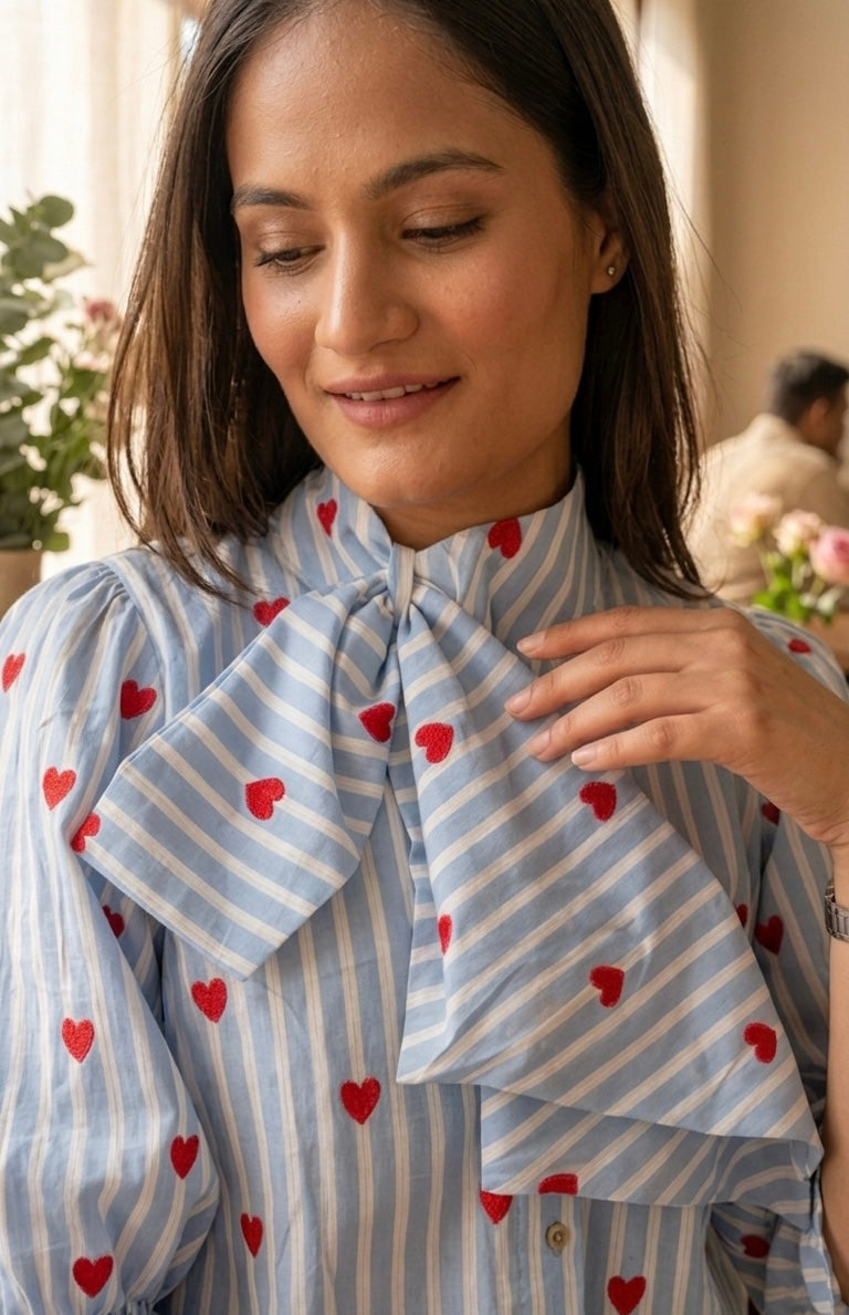 Woman wearing a light blue striped shirt with red heart patterns, adjusting her collar.