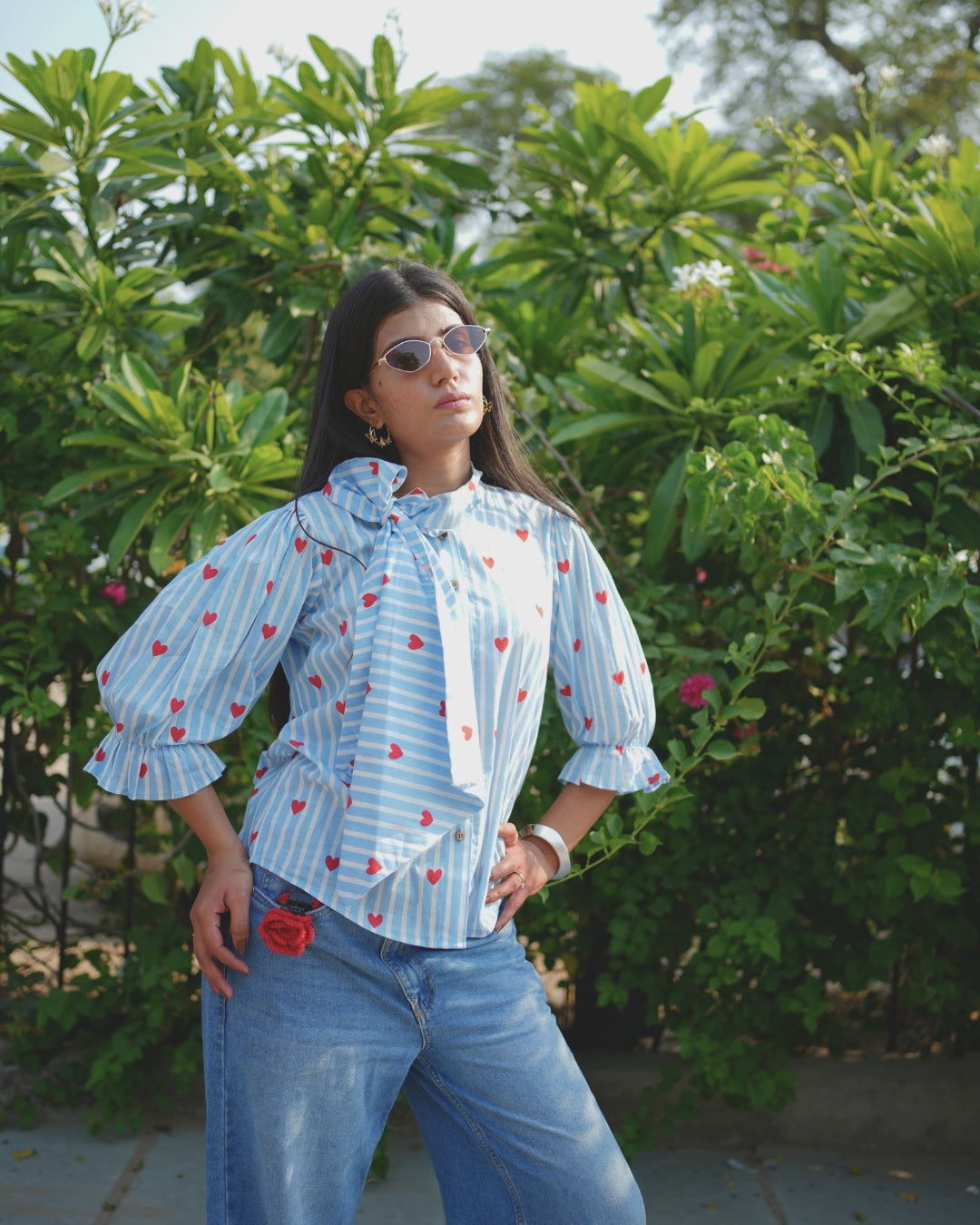 Woman wearing a blue patterned blouse and jeans standing in a garden.