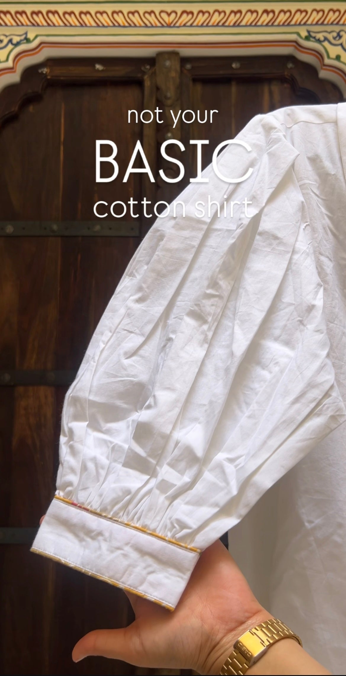 White cotton shirt held by a hand with gold trim against a wooden background