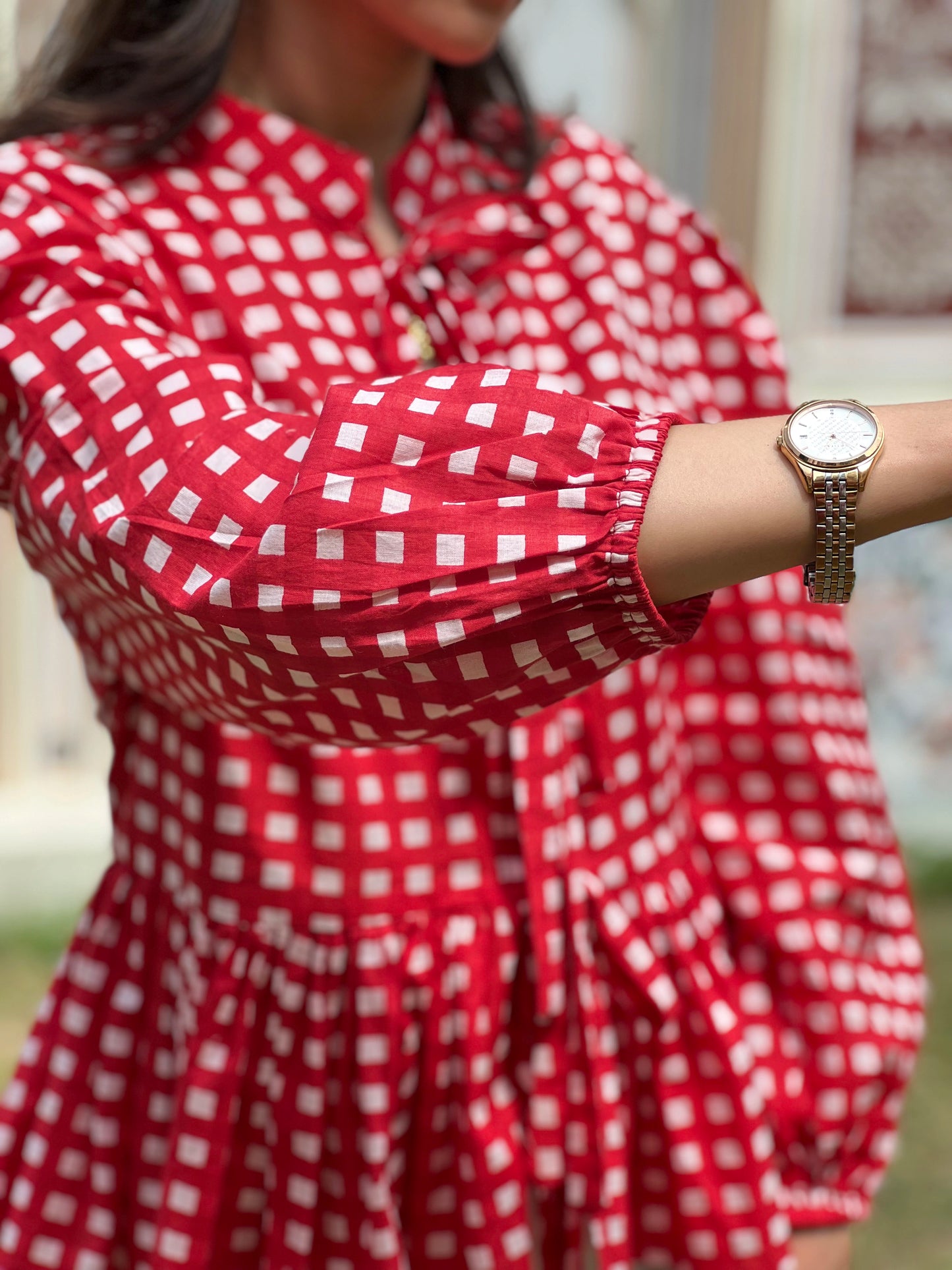 Person wearing a red and white checkered dress with a gold watch.