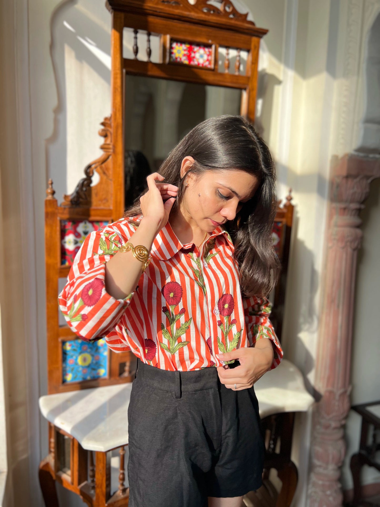 Woman adjusting her hair in a room with a mirror and decorative items.