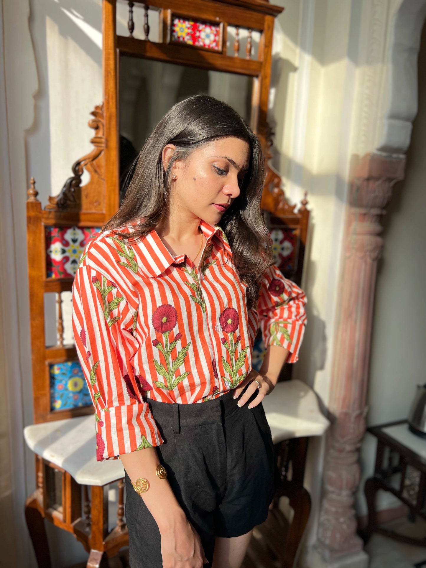 Woman wearing a red and white striped shirt with floral patterns in an indoor setting.
