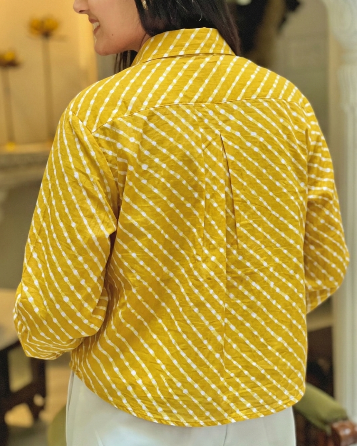 A woman shown from the back wearing a yellow and white striped shirt with diagonal dotted lines, paired with white pants in an indoor setting.