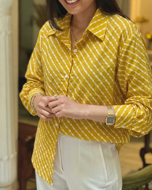 A woman wearing a yellow and white patterned button-up shirt with white pants, shown from the chest down in an indoor setting.